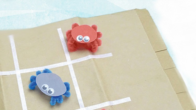 Zwei Bastelkrabben aus Pfeifenreinigern mit Wackelaugen, eine rot, eine blau, auf einem selbstgebastelten Tic-Tac-Toe-Feld aus Pappe.