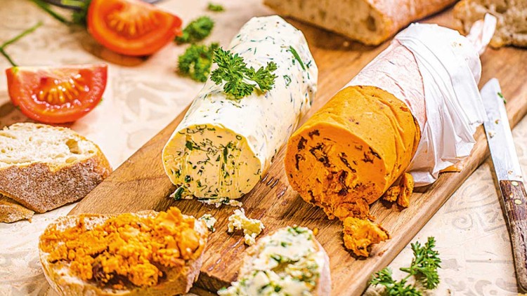 Zwei Baguettestücke mit Kräuterbutter und Tomatenbutter auf einem Holzbrett, daneben Tomatenstücke und Petersilie.