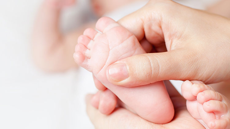Eine Hand hält zwei kleine Babyfüße vor unscharfem weißem Hintergrund.