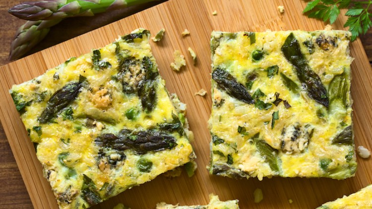 Zwei rechteckige Stücke Frittata mit grünem Spargel, Erbsen und Kräutern auf einem Holzbrett, daneben frische Spargelspitzen.