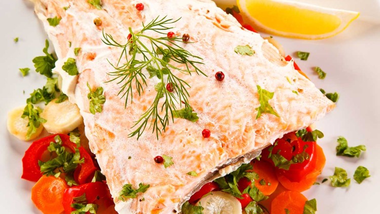Gegarter Lachs auf einem Bett aus geschnittenem Gemüse wie Karotten und Paprika, dekoriert mit Kräutern, Pfefferkörnern und Zitrone.