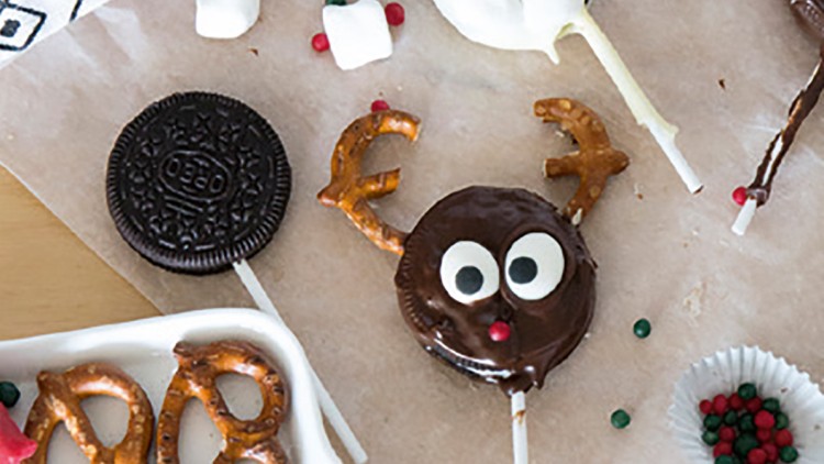 Gebäck-Lollis in Rentier- und Weihnachtsdesign liegen auf Backpapier, mit Schokolade, Brezeln und Marshmallows verziert.
