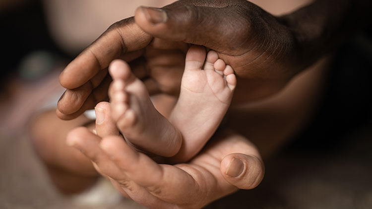 Erwachsene Hände halten vorsichtig die kleinen Füße eines Babys, Hintergrund unscharf.