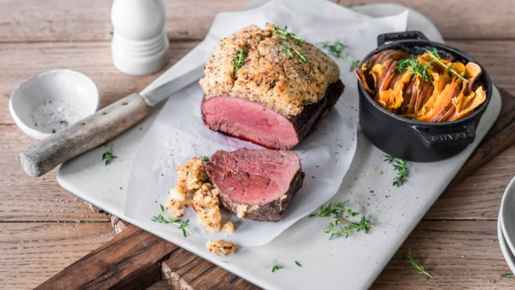 Aufgeschnittenes Rinderfilet in Kräuterkruste mit Beilage aus geschichteten Süßkartoffeln in einer schwarzen Auflaufform.
