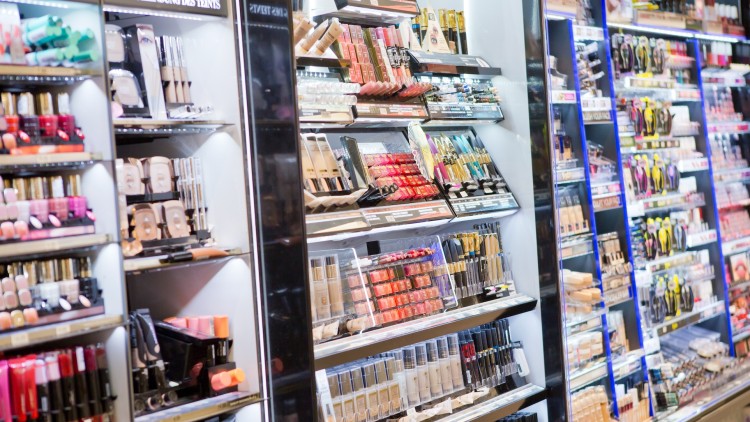 Regale mit Kosmetikartikeln wie Lippenstiften, Nagellacken, Foundations und Make-up-Tools in einem Geschäft.