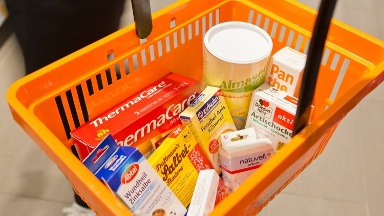 Oranger Einkaufskorb mit Produkten wie ThermaCare, Zinksalbe, Artischocken-Kapseln, Salbeitee und einer Dose Alnatura Sojadrink.