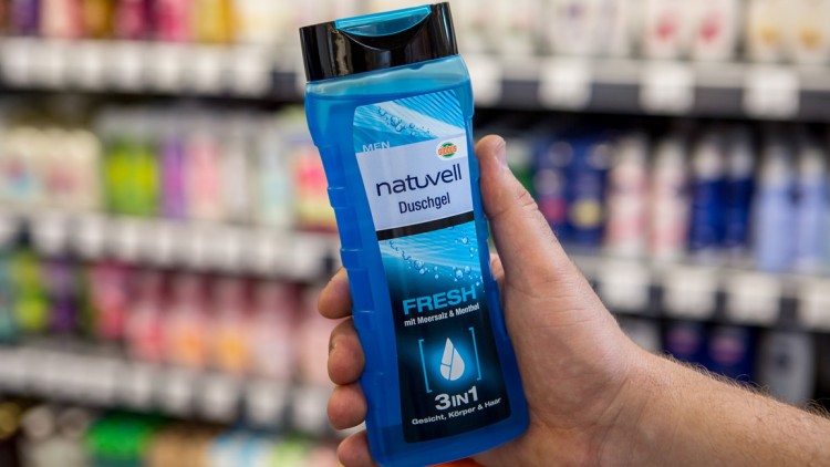 Eine Hand hält eine blaue Flasche „natuvell Duschgel Fresh mit Meersalz & Menthol 3in1“ vor einem Regal mit Duschgel.