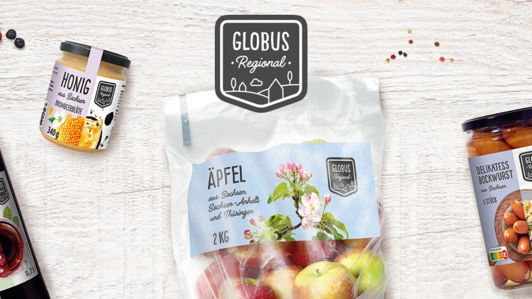 Flasche Sauerkirschnektar, Glas Brombeerblütenhonig, Beutel Äpfel und Glas Bockwurst von GLOBUS Regional auf Holzuntergrund.