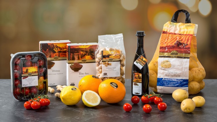 Auf einem Tisch stehen GLOBUS Gold-Produkte wie Kartoffeln, Wildreis, roter Reis, Erdnüsse, Öl, Cocktailtomaten, Orangen und Zitronen.