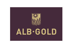 Logo mit cremefarbenem Schriftzug ALB•GOLD auf dunkelviolettem Hintergrund und Emblem mit Sonne und Getreideähren.