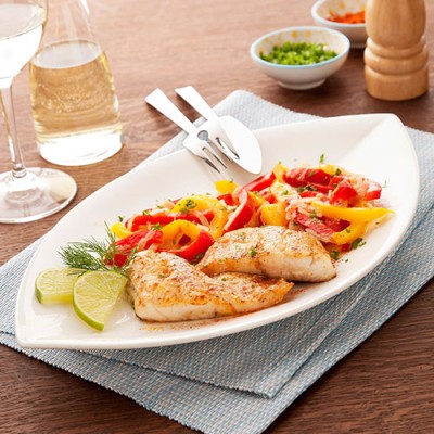 Gegrilltes Fischfilet mit Paprikastreifen und Kräutergarnitur auf weißem Teller, daneben Limetten und Besteck.