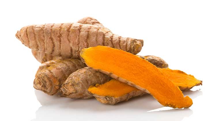 Mehrere braune Kurkuma-Wurzeln mit sichtbaren orangefarbenen, frisch geschnittenen Scheiben liegen auf einer glänzenden Fläche.