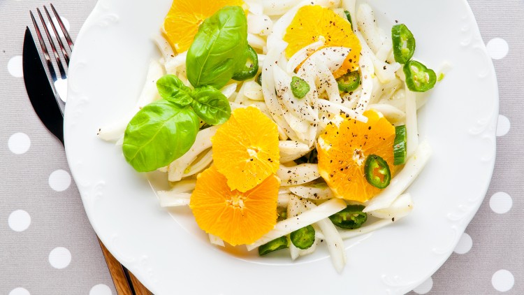Ein weißer Teller mit Fenchel, Orangenscheiben, grünen Chiliringen, frischem Basilikum und schwarzem Pfeffer.