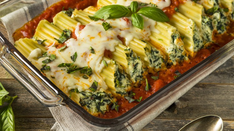 Gefüllte Cannelloni mit Spinat und Käse in Tomatensoße, garniert mit frischem Basilikum, in einer gläsernen Auflaufform.