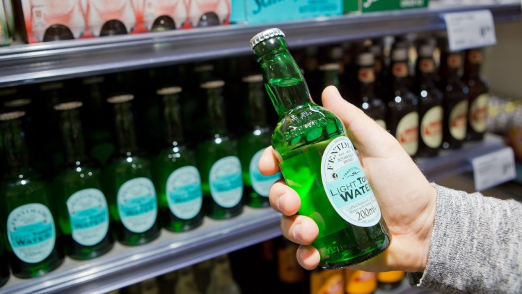 Eine Hand hält eine grüne Glasflasche mit der Aufschrift „Fentimans Light Tonic Water 200 ml“ vor einem Getränke-Regal.