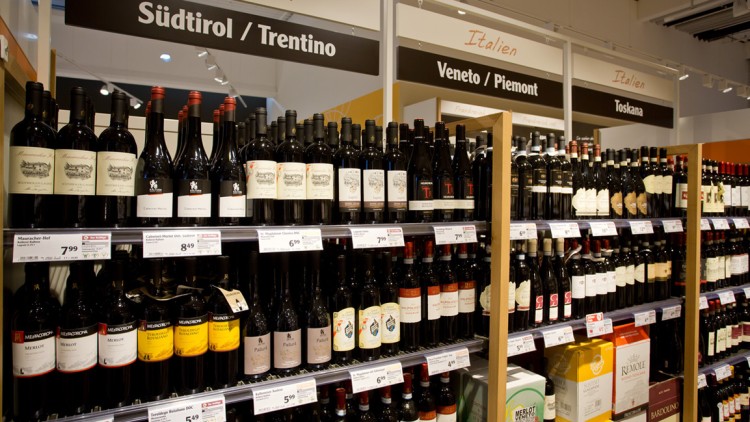 Ein Weinregal mit Flaschen aus Südtirol, Venetien und der Toskana, darüber schwarz-weiße Schilder mit den Regionenamen.