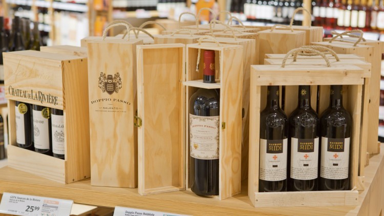 Mehrere Holzgeschenkkisten mit Weinflaschen, darunter Aufschriften wie „Chateau de la Riviere“, „Doppio Passo“ und „Saveurs Midi“.