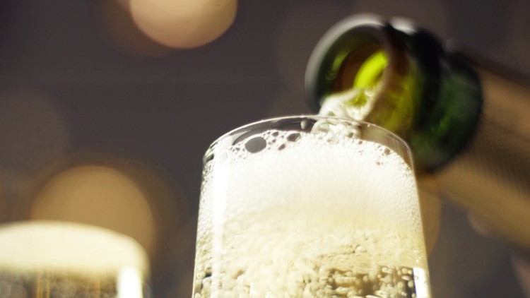 Ein Glas wird mit sprudelndem Getränk aus einer geöffneten, grünlichen Flasche gefüllt, im Hintergrund warme Lichter.