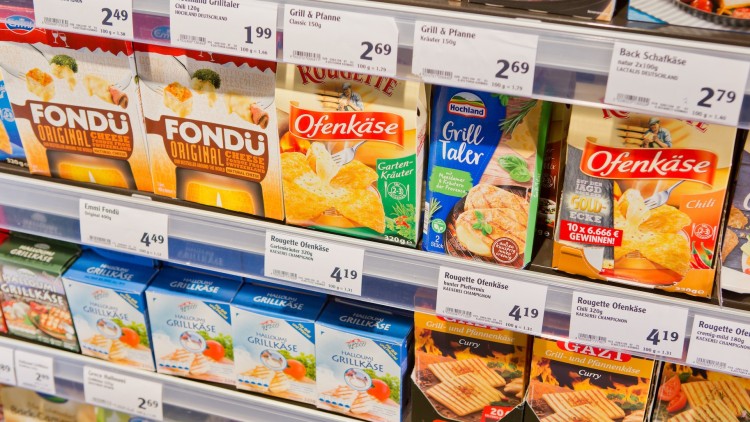 Regal mit verschiedenen Käseprodukten wie Fondu, Ofenkäse und Grilltaler, Preisschilder sind über und unter den Produkten sichtbar.