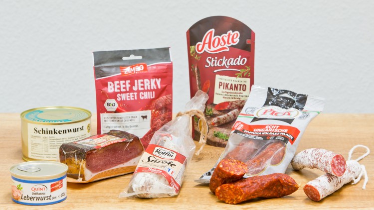 Verschiedene Wurst- und Fleischprodukte wie Schinkenwurst, Salami und Beef Jerky auf einer Holzoberfläche platziert.