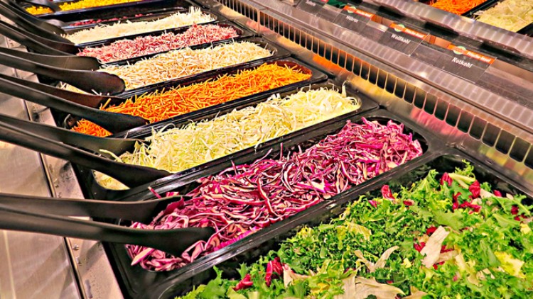 Mehrere Schalen mit frisch geschnittenem Salat und Gemüse wie Rotkohl, Karotten und Blattsalat in einer Salatbar.