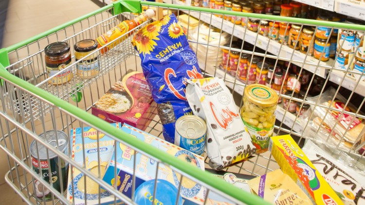 Ein Einkaufswagen mit Lebensmitteln wie Chips, Couscous, Okra im Glas, Dosen, Soßenflasche und verschiedenen Verpackungen.