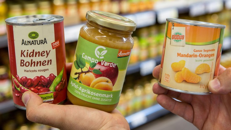Drei Hände halten je ein Produkt: Alnatura Kidney Bohnen, Campo Verde Apfel-Aprikosenmark und GLOBUS Mandarinen-Orangen.