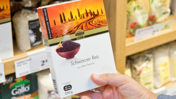 Hand hält eine Packung „GLOBUS Gold Schwarzer Reis aus dem Piemont, 250 g“ vor einem Verkaufsregal mit weiteren Reisprodukten.