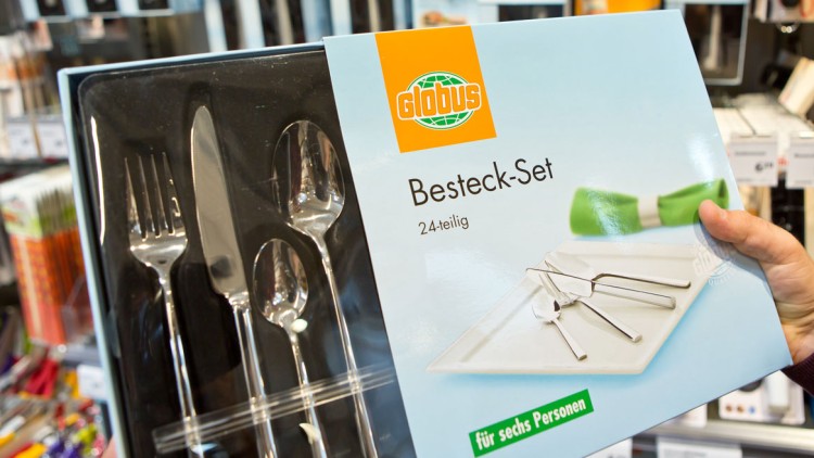 Verpackung eines 24-teiligen Besteck-Sets von GLOBUS für sechs Personen, abgebildet mit Messer, Gabel und Löffel auf Serviette.
