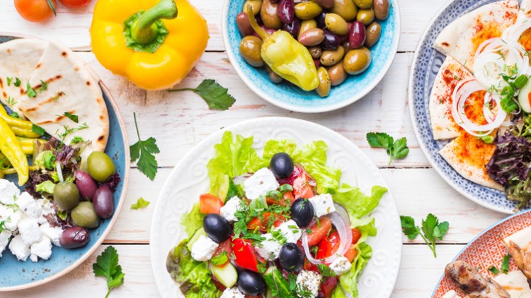 Verschiedene mediterrane Gerichte wie Kebabs, Salat, frittierten Fisch, Fladenbrot, Tzatziki und Oliven auf Holztisch.