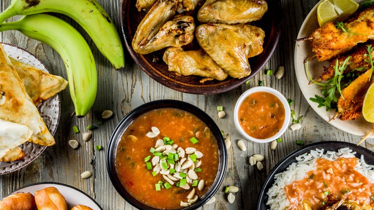 Verschiedene Gerichte wie Reis, Suppe, Hähnchenspieße, Teigtaschen, Chicken Wings, Bananen und Soßen auf Holztisch.