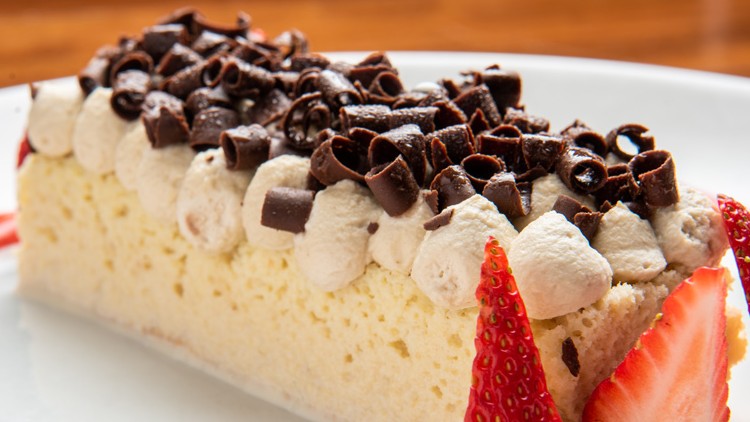 Ein rechteckiges Dessert mit Sahne, Schokoraspeln und frischen Erdbeerstücken auf einem Teller mit roter Soße.