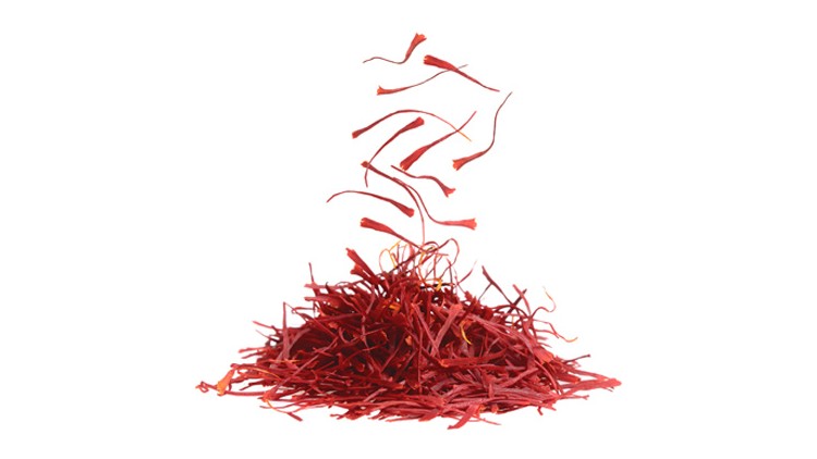 Rote Safranfäden liegen in einem kleinen Haufen, umgeben von einigen lose in der Luft schwebenden Fäden auf weißem Hintergrund.