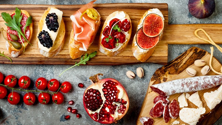 Verschiedene belegte Brotscheiben mit Obst, Rucola und Schinken sowie Granatapfel, Tomaten, Wurst und Käse auf Holzunterlagen.