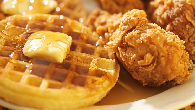 Zwei goldbraune Waffeln mit Butter und Sirup neben knusprig panierten Hähnchenteilen auf einem weißen Teller.