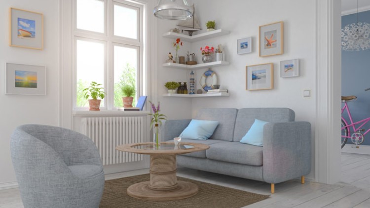 Helles Wohnzimmer mit grauem Sofa, blauen Kissen, Sessel, rundem Couchtisch, Fenster mit Pflanzen und weißen Wandregalen.