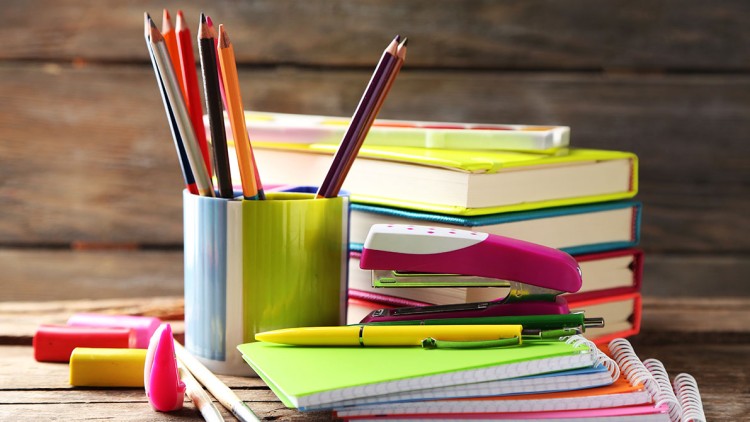 Stapel bunter Notizbücher, Stiftehalter mit Buntstiften, pinker Tacker und weitere Schreibwaren auf Holztisch.