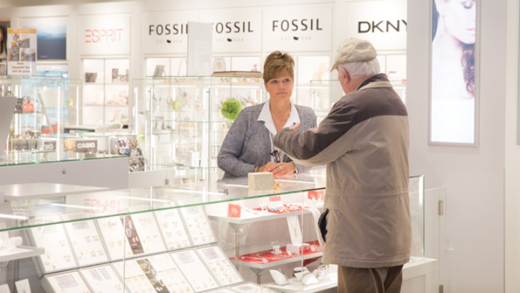 Ein älterer Mann steht an einer Glasvitrine mit Schmuck, dahinter stehen Marken wie ESPRIT, FOSSIL und DKNY.