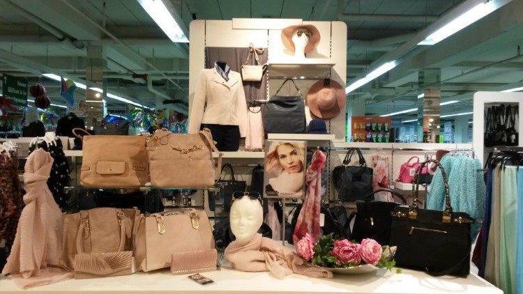 Verschiedene Handtaschen, Accessoires, Schals und Kleidung in Beige-, Rosa- und Schwarztönen auf einem weißen Präsentationstisch.
