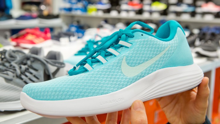 Türkiser Sportschuh mit weißer Sohle und sichtbarem „Lunarlon“-Schriftzug wird vor einem Regal mit weiteren Sportschuhen gehalten.