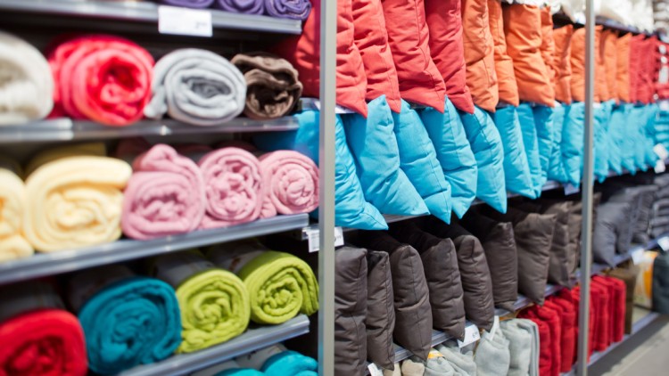 Regale mit zusammengerollten Decken in verschiedenen Farben und Kissen in Blau, Grau, Orange und Rot.