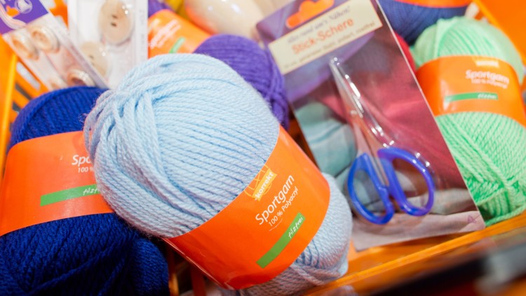 Mehrere Knäuel Sportgarn in verschiedenen Farben, Stickschere und Knöpfe liegen in einem orangefarbenen Korb.
