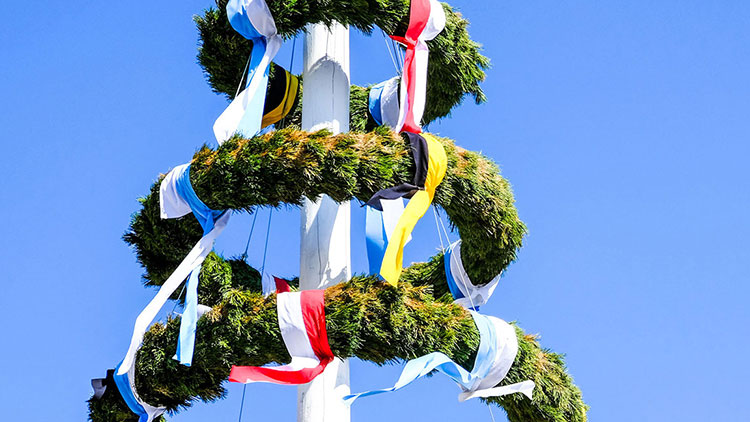 Ein geschmückter Maibaum mit grünen Girlanden und bunten Bändern vor klarem, blauem Himmel.