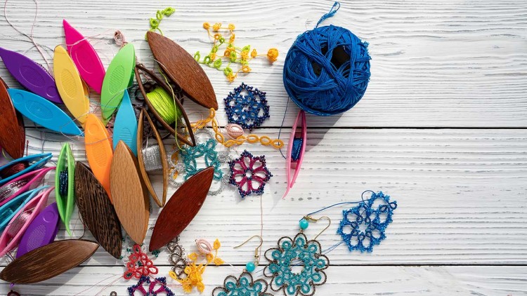 Verschiedene bunte Occhi-Schiffchen, Garn, Spitze und handgefertigte Spitzenmuster aus Perlen auf weißem Holztisch.