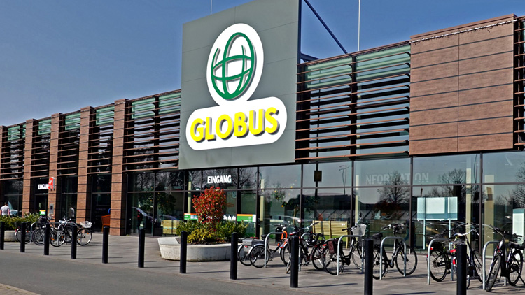 Die Außenfassade eines GLOBUS Marktes mit Glasfront, Holzverkleidung, großem GLOBUS Logo und Eingangstür mit „Eingang“-Schild.