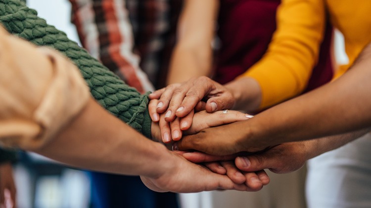 Mehrere Hände unterschiedlicher Personen liegen übereinander, Symbol für Gemeinschaft und Zusammenarbeit.