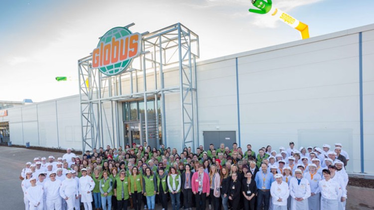 Eine große Gruppe von Personen in Arbeitskleidung steht vor einem GLOBUS-Markt mit sichtbarem Logo und Globini-Maskottchen am Himmel.