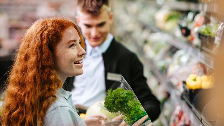 Person hält ein Bündel frische Petersilie in einer durchsichtigen Verpackung in der Gemüseabteilung eines Supermarkts.