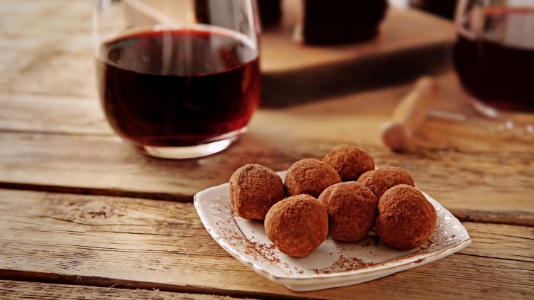 Ein Glas Rotwein und ein Teller mit Pralinen in Kakaopulver auf einer hölzernen Tischoberfläche.