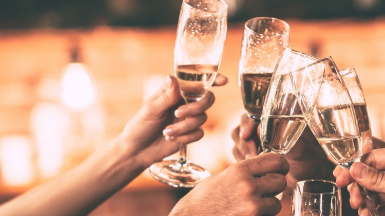 Mehrere Hände stoßen mit gefüllten Champagnergläsern in einer warm beleuchteten Umgebung an.
